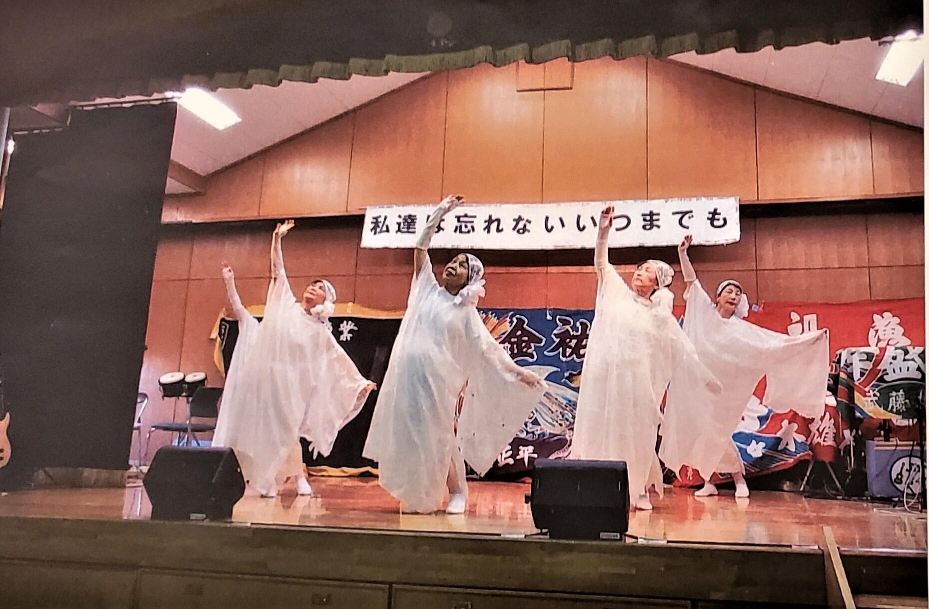 舞台上で白の衣装を身にまとった女性たちが踊っている