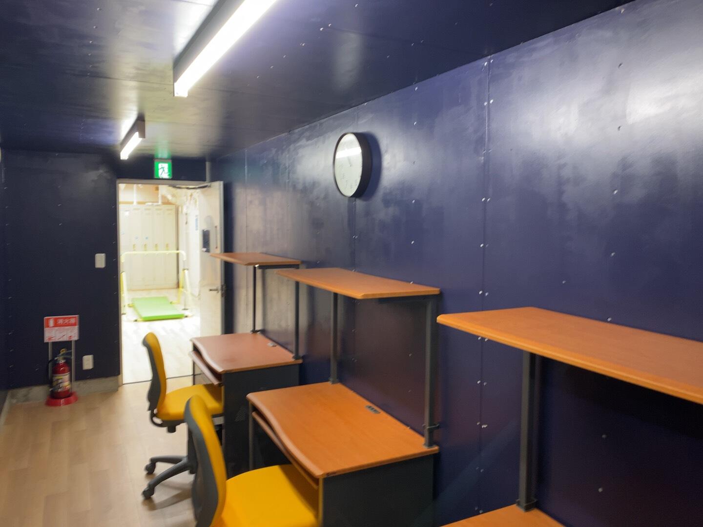 黒い壁面の前に勉強机と椅子が3点ずつ置かれている