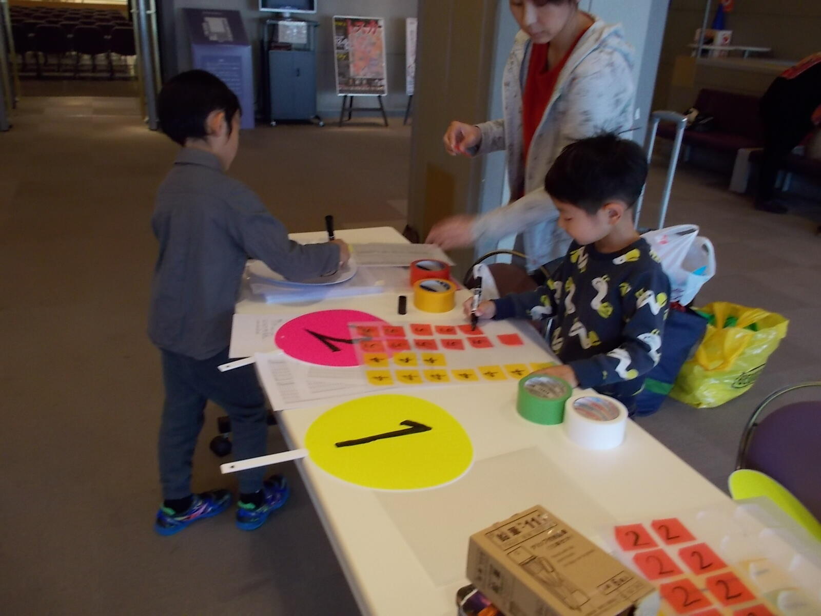 子どもたちが、うちわと色のついたテープにマジックで数字を書いて、楽器体験の準備をしている。