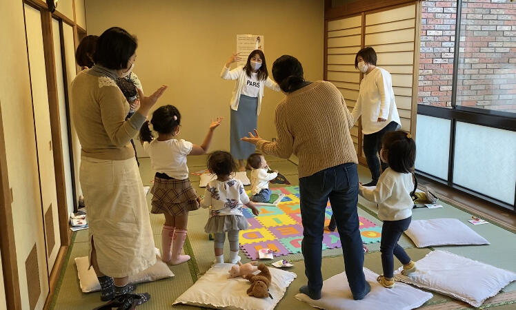 幼児と大人の女性たちが両手を広げて、遊びながら英語を学んでいる