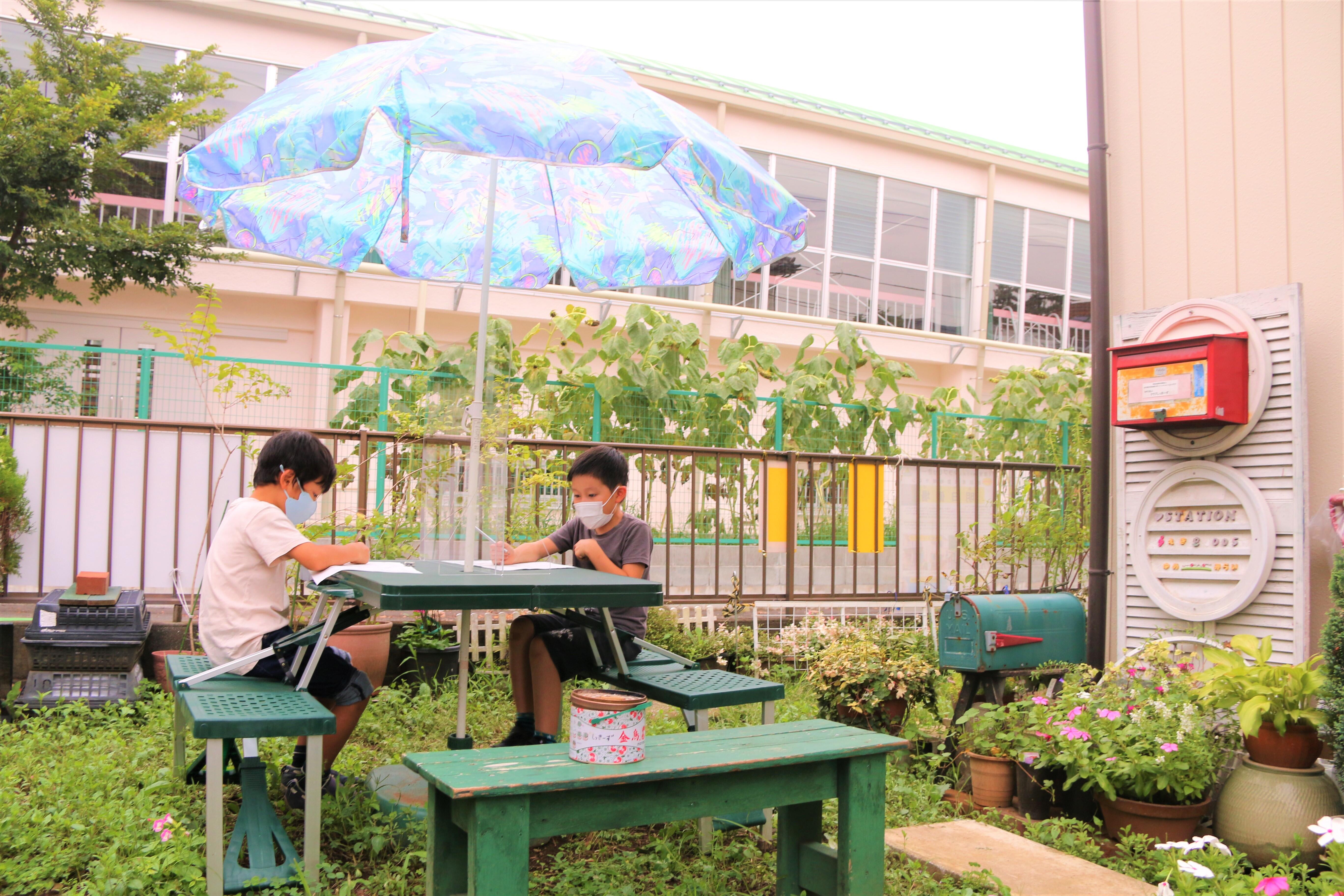 庭に机と椅子を出して宿題をしている男子小学生二人
