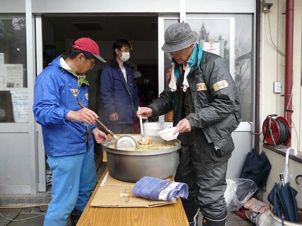 男性二人が鍋の中のスープをお椀にすくっている