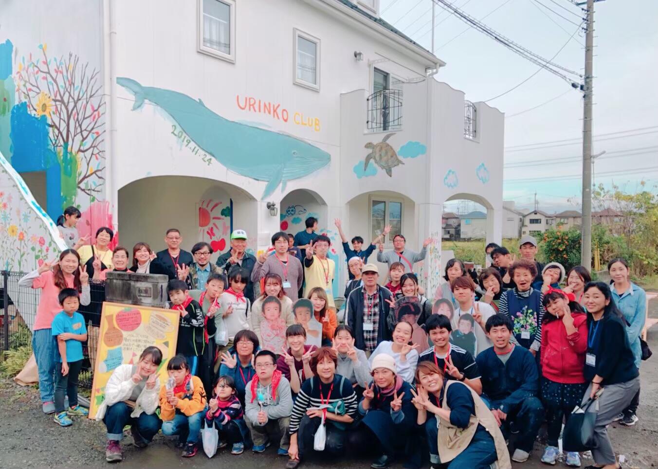 クジラやカメなどの絵が描かれた家を前に参加者と記念撮影。