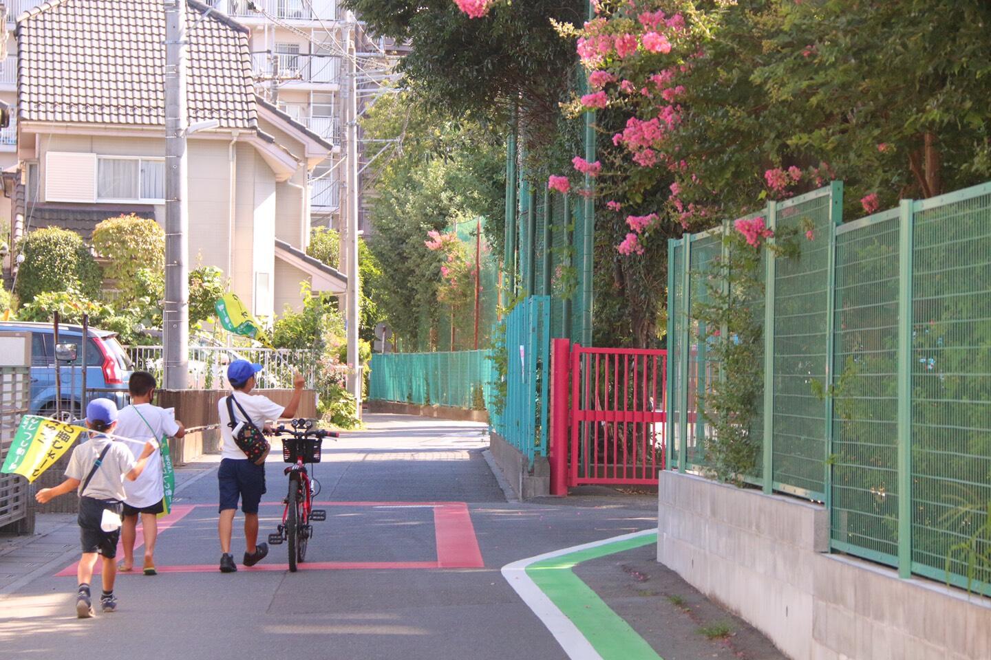 小学校前の道路をクラブしっきーずの小旗とチラシを持って歩く小学生の男の子3人