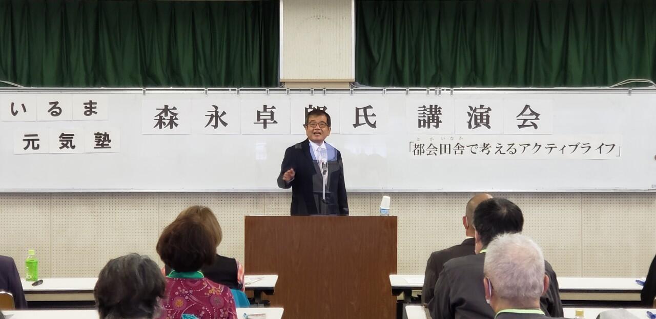 大勢の参加者の前で森永卓郎氏が話をしている。